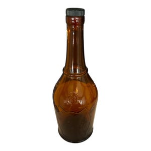 May include: Amber glass bottle with a black cap. The bottle features a long neck and a rounded base with a decorative pattern. The glass has a glossy finish. The bottle is empty.