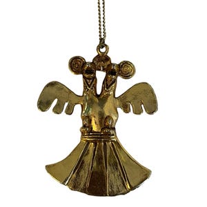 May include: Gold-toned pendant necklace featuring a stylized double-headed bird design. The pendant has outstretched wings and a flared skirt-like bottom. The necklace chain is a delicate, matching gold color, creating a cohesive and elegant accessory.
