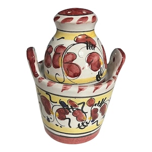 May include: A ceramic salt and pepper shaker set. The set features a white base with red and yellow floral designs. The salt shaker has a red top and the pepper shaker sits in a matching holder with handles.