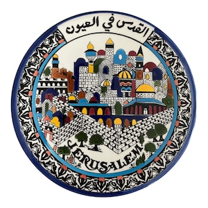 May include: A round, decorative ceramic plate with a detailed illustration of Jerusalem. The plate features a blue border and a central image of the city with colorful buildings, domes, and the word "Jerusalem" in English.