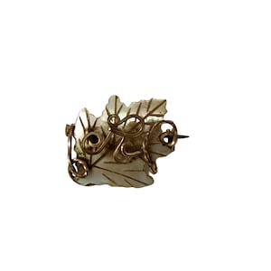 May include: A vintage leaf-shaped brooch with a mother-of-pearl appearance. The brooch features a gold-toned wire design overlaying the leaf, with a pin on the back for secure fastening. The design is intricate and detailed.
