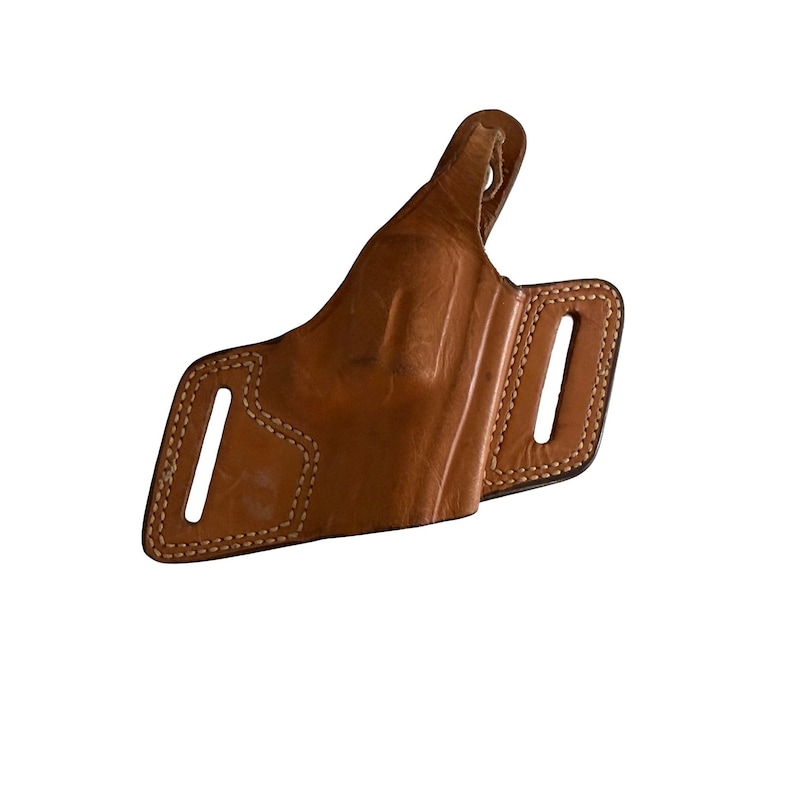 Puede incluir: Una funda de cuero marr&oacute;n con costuras visibles y dos ranuras para cintur&oacute;n. La funda est&aacute; dise&ntilde;ada para llevarse en la cadera y tiene un lazo para sujetarla al cintur&oacute;n. El cuero tiene un aspecto desgastado.