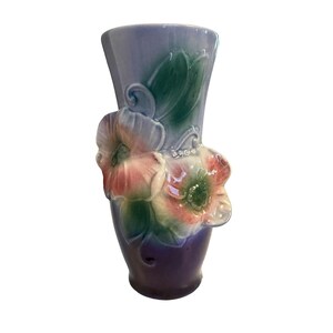 May include: A ceramic vase featuring a gradient colour scheme that transitions from a deep purple base to a light lavender top. The exterior is decorated with three-dimensional sculpted flowers in shades of pink, green, and white with a glossy finish.