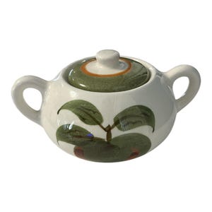 May include: A white ceramic sugar bowl with a lid and two handles. The lid is green with an orange band, and the bowl is decorated with green leaves and brown accents. A charming addition to any kitchen.