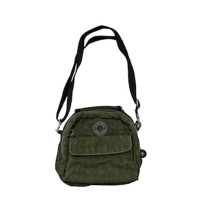 May include: Olive green crossbody bag with a black adjustable strap. The bag has a front pocket and a circular logo patch. The bag is made of a crinkled nylon material.