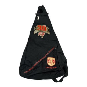 May include: Black sling backpack featuring the Tampa Bay Buccaneers logo and the Dodge logo. The backpack has a zippered top and a strap with the text "An Official Vehicle of the Tampa Bay Buccaneers". The backpack also has a patch that says "30 Seasons 1976-2005".