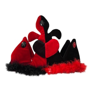 May include: A jester-style crown crafted from red and black velvet fabric. The crown features a central fleur-de-lis shape, pointed side panels, and is adorned with black and red faux fur trim along the base, plus small embedded dark gems.