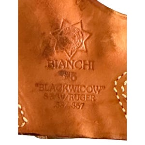 Puede incluir: Primer plano de una funda de cuero marr&oacute;n con el texto en relieve "BIANCHI" y "BLACKWIDOW" junto con "S&W/RUGER .38/.357". La funda presenta un dise&ntilde;o decorativo de estrella y costuras blancas.