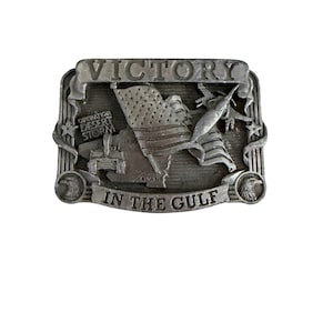 May include: A rectangular, silver-colored belt buckle with the word "VICTORY" at the top. The buckle features an American flag, a map, and the text "IN THE GULF" at the bottom. The words "Operation Desert Storm" are also visible.