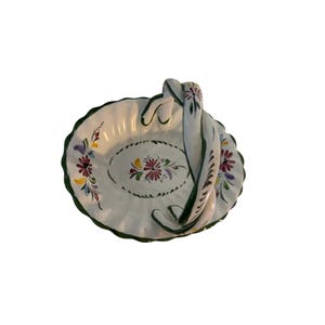May include: A white ceramic basket with a scalloped edge and a curved handle. The piece features hand-painted floral motifs in red, yellow, and green, with a green painted rim. The interior and handle are decorated with small, colorful flower designs.