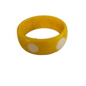 May include: A bright yellow bangle bracelet featuring a smooth, polished surface with evenly spaced, circular white polka dot patterns around the exterior. The circular accessory has a thick, rounded band design with a consistent width throughout.