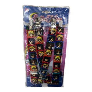 May include: A pair of suspenders featuring a repeating pattern of anime character portraits in red, blue, and yellow. The suspenders have silver-colored metal clips and are packaged in a clear plastic bag with the words "Sailor Moon".