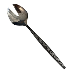 Puede incluir: Un tenedor de ensalada plateado con una cabeza ranurada y un mango largo. El mango está decorado con un patrón floral grabado. El tenedor está diseñado para servir ensaladas y otros platos.