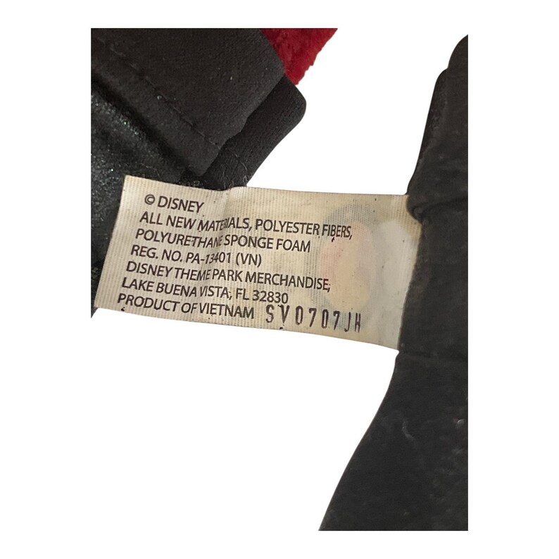 Puede incluir: Primer plano de una etiqueta de producto de Disney. La etiqueta incluye el logotipo de Disney, informaci&oacute;n sobre los materiales y el texto "DISNEY THEME PARK MERCHANDISE, LAKE BUENA VISTA, FL 32830". El producto est&aacute; fabricado en Vietnam.