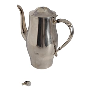 May include: A silver-colored coffee pot with a curved spout and handle. The pot has a lid and a rounded body. A small, decorative object is at the bottom of the image.