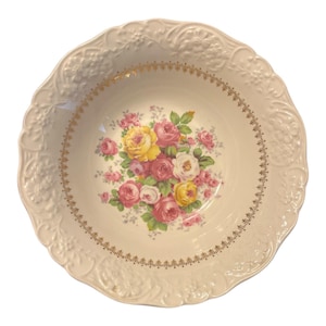 Puede incluir: Bol de porcelana crema, vintage, con borde festoneado y detalles florales en relieve. El bol presenta un ramo floral central en tonos rosa, amarillo y blanco, acentuado con ribete dorado. Una pieza decorativa para servir.