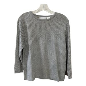 Può includere: Un maglione grigio a maniche lunghe con scollo tondo. Il maglione ha un design a maglia aperta strutturata ed è appeso a una gruccia di plastica trasparente. Il marchio "alfred dunner" è visibile sull'etichetta.