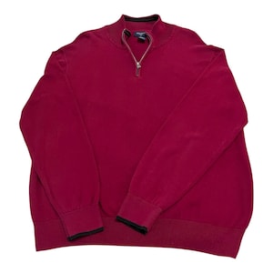 May include: A burgundy zip-up sweater with a ribbed hem and cuffs. The sweater has a mock neck and a silver zipper. The cuffs have a black trim. The sweater is made of a soft material.