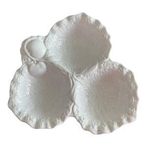 Puede incluir: Plato de cerámica blanca para servir en forma de hoja con tres secciones. El plato tiene una superficie texturizada con detalles de venas de hojas y un pequeño acento de manzana. Los bordes son festoneados.