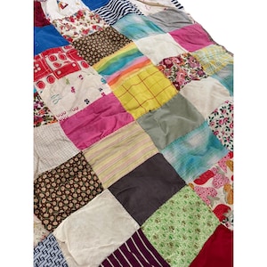 May include: A patchwork quilt constructed from various fabric squares featuring diverse patterns and colors, including floral prints, stripes, solid pink, yellow, brown, and blue sections, stitched together in a grid arrangement.
