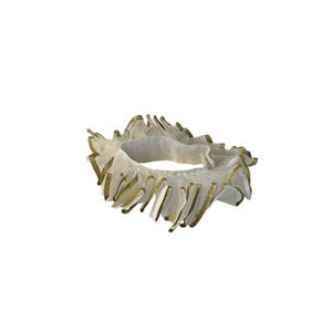May include: A white, ruffled accessory with gold glitter trim. The circular design features multiple layers of delicate fabric, creating a textured, decorative effect. The gold accents add a touch of sparkle to the piece.