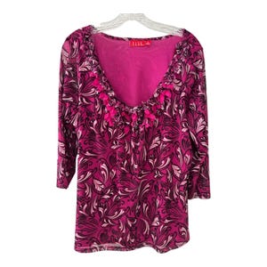 May include: A magenta blouse with a black and white floral design. The top features three-quarter length sleeves and a scoop neckline, trimmed with pink fabric. The brand label "ELLE" is visible.