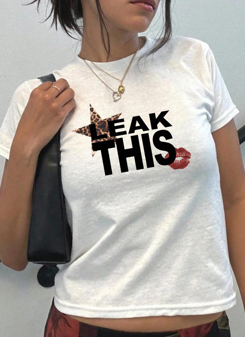 May include: White t-shirt featuring the text "LEAK THIS" in black. A star with a leopard print pattern is above "LEAK", and a red lipstick kiss graphic is beside "THIS".
