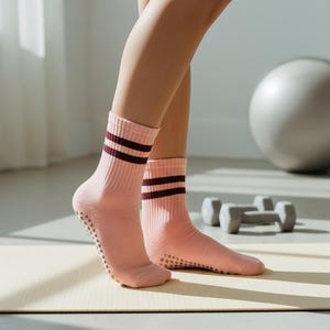 Könnte beinhalten: Rosafarbene Sportsocken mit zwei weinroten Streifen am oberen Rand und gepunkteten Griffen an den Sohlen. Die Socken werden während eines Workouts getragen, mit einer Yogamatte, Hanteln und einem Gymnastikball im Hintergrund.