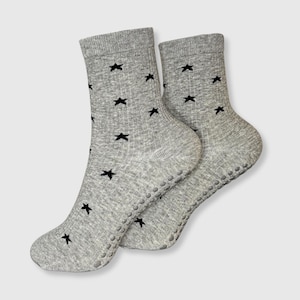Könnte beinhalten: Ein Paar graue Socken mit schwarzen Sternmustern. Die Socken haben eine gerippte Textur und kleine, graue Anti-Rutsch-Griffe an den Sohlen. Hergestellt aus einem weichen, bequemen Material.