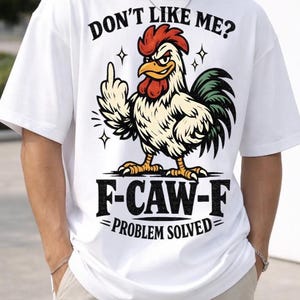 May include: White t-shirt featuring a cartoon rooster illustration giving the middle finger. The text above reads "DON'T LIKE ME?" and below the rooster is "F-CAW-F = PROBLEM SOLVED=". The rooster is coloured red, yellow, green, and white.