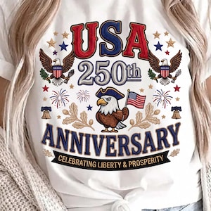 Może przedstawiać: Biała koszulka z patriotycznym wzorem upamiętniającym 250. rocznicę USA. Zawiera napis "USA 250th Anniversary" z orłami, gwiazdami i orłem w kapeluszu trzymającym flagę. Zawiera również frazę "Celebrating Liberty & Prosperity".