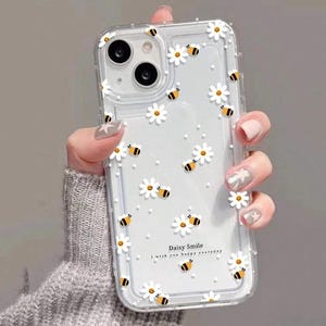 May include: Clear phone case with a white daisy and bee design. The case has the text "Daisy Smile I wish you happy everyday".