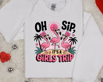 May include: White sweatshirt featuring a graphic of three pink flamingos wearing sunglasses and bows, with the text "OH Sip, IT'S A GIRLS TRIP". The design includes palm trees, a pink sun, and stars.