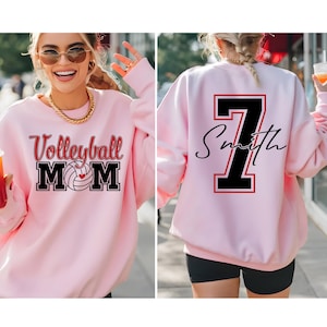 Peut inclure: Un sweat-shirt rose clair avec l'inscription "Volleyball MOM" en rouge et noir sur le devant. Le dos du sweat-shirt porte un grand chiffre 7 noir avec un contour rouge et le nom "Smith" en &eacute;criture cursive.