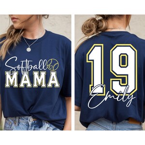 May include: A navy blue t-shirt with the text "Softball Mama" and a softball graphic on the front. The back of the shirt has a white number 19 with a yellow outline and the name "Emily" written in cursive below the number.