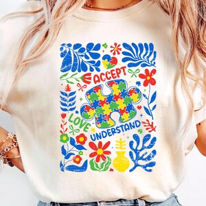 May include: White t-shirt with a colorful puzzle piece design and the words "Accept, Love, Understand".