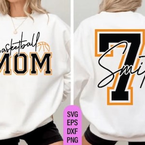 May include: White sweatshirt with the text "Basketball MOM" in black and orange lettering on the front. The back features the number 7 in black with an orange outline and the name "Smith" in script.