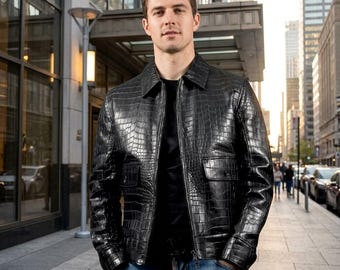 May include: A black leather jacket with a glossy crocodile skin texture, featuring a pointed collar, a full-length front zipper, and two flap pockets on the chest. The jacket is worn over a plain black shirt and blue denim jeans in an urban setting.