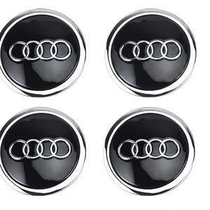 May include: Four black and silver car wheel centre caps. Each cap features the Audi logo, a set of four interlocking rings, in silver against a glossy black background. The caps have a silver trim.