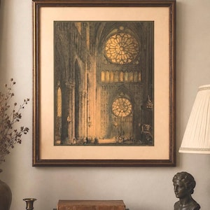 May include: Framed print of a cathedral interior with large stained glass windows. The print is in a dark brown wooden frame and is displayed on a table with books, a bust, and a lamp.