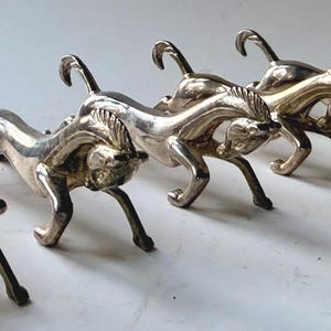May include: A set of five silver-colored metal horse figurines in a running pose. The horses have detailed manes and tails, with their legs extended as if in motion. The figurines are arranged in a row.