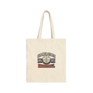 Peut inclure: Sac fourre-tout crème avec un motif de basket-ball. Le motif présente le texte "SOONER STATE" au-dessus d'un graphique de basket-ball, avec "OK" et "WEST" de chaque côté. En dessous, le mot "BASKETBALL" en rouge, de style vintage.