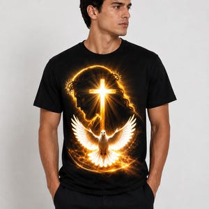 Puede incluir: Una camiseta negra de manga corta con un estampado gráfico de una cruz dorada brillante, la silueta de una cabeza con una corona de espinas y una paloma blanca con las alas extendidas, todo rodeado por un círculo de luz dorada intensa.