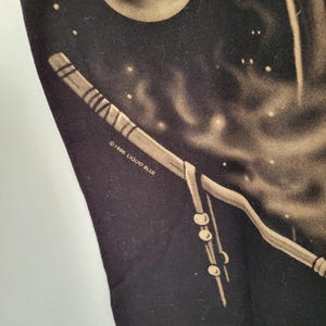 May include: Black t-shirt featuring a celestial design with a full moon and a stylized staff. The design includes a night sky with stars and the text "&copy;1996 LIQUID BLUE". The artwork is in shades of tan and white.