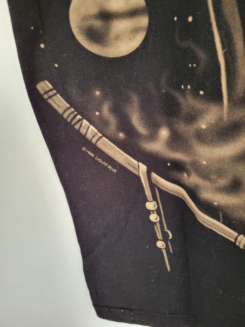 May include: Black t-shirt featuring a celestial design with a full moon and a stylized staff. The design includes a night sky with stars and the text "&copy;1996 LIQUID BLUE". The artwork is in shades of tan and white.