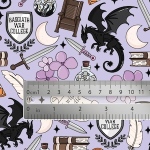 May include: A light purple fabric featuring a repeating pattern of black dragons, swords, shields labeled Basgiath War College, books, moons, and flowers. A metal ruler is placed across the center, showing measurements in inches and centimeters.