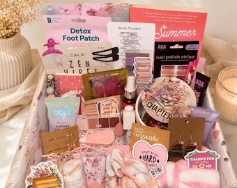 May include: A gift box filled with assorted items including a pink book titled Summer, a Detox Foot Patch, AOA nail polish strips, a book tracker card, a shower steamer, a small makeup palette, earrings, a pink scrunchie, and various stickers.