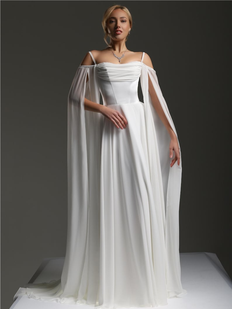 May include: A white wedding dress with a flowing skirt and off-the-shoulder straps. The dress has a fitted bodice and a long, flowing train.