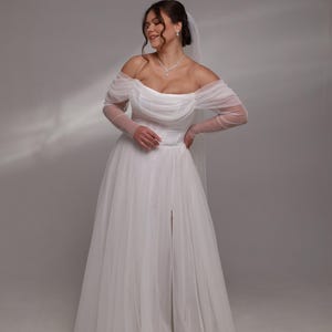 May include: A white off-the-shoulder wedding dress with long sheer sleeves and a slit in the skirt.