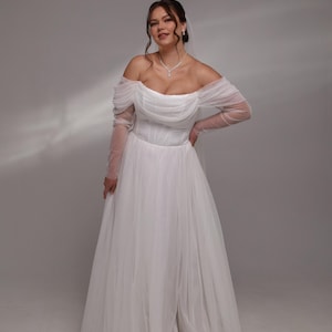 May include: A white off-the-shoulder wedding dress with long sleeves and a flowing skirt.